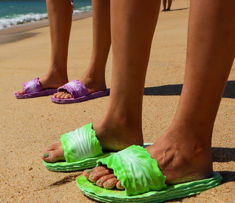 Two people wearing Coddies Cabbage Creepers on the beach, one green and one purple